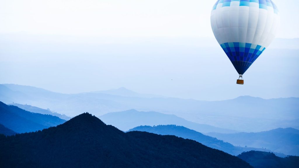 Blue and white hot air balloon traveling over mountains