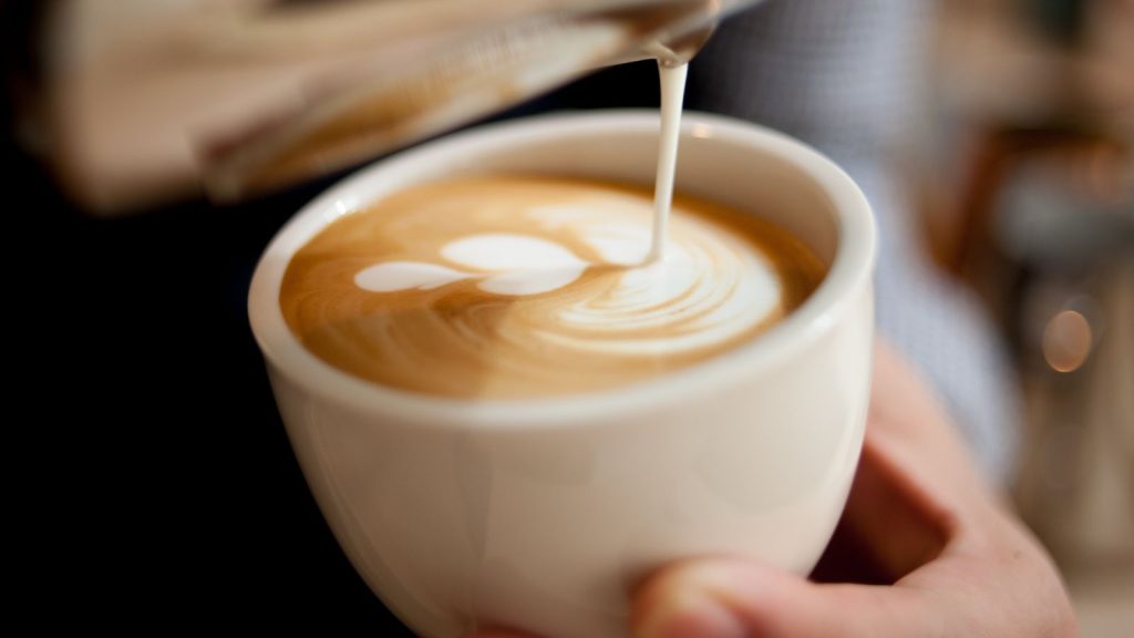 milk being poured into an espresso making a latte with a leaf design