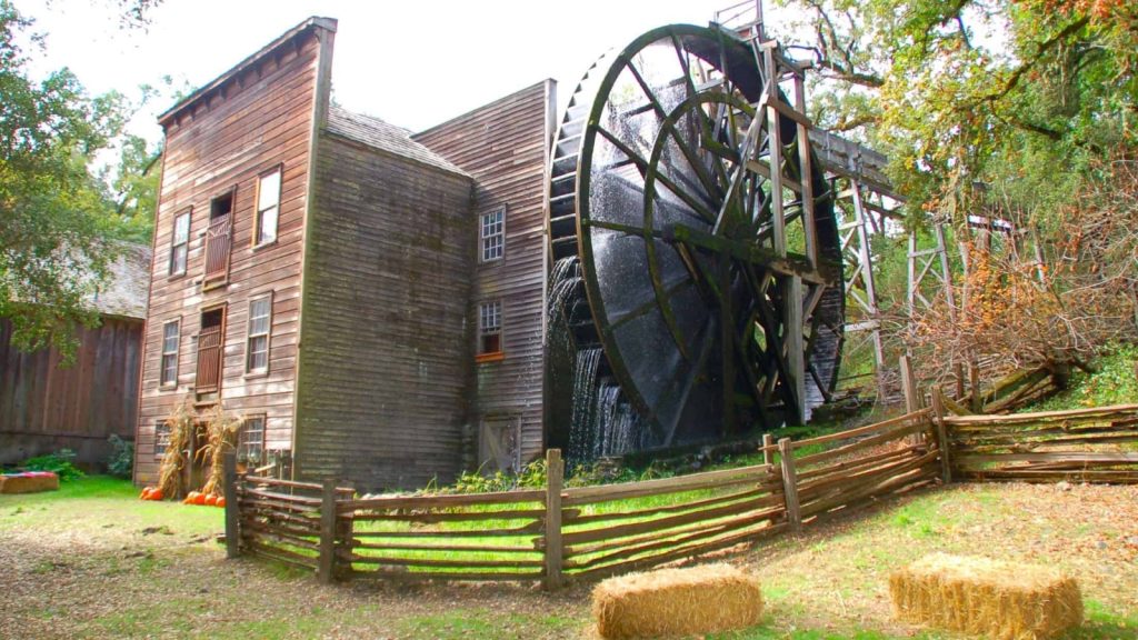 Bale Grist Mill Historic Park showcases the restored 19th-century wooden grist mill with its iconic large water wheel surrounded by rustic wooden fencing and peaceful grounds