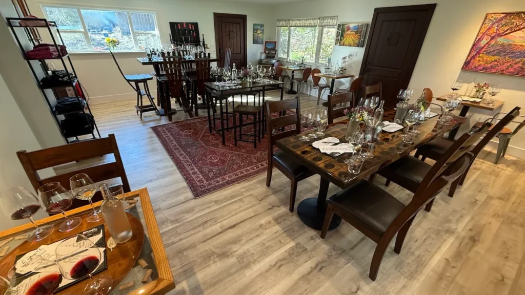 Elegant interior tasting room at Bougetz Cellars featuring multiple dining tables set with wine glasses, extensive wine bottle displays, and sophisticated decor creating an upscale wine tasting atmosphere