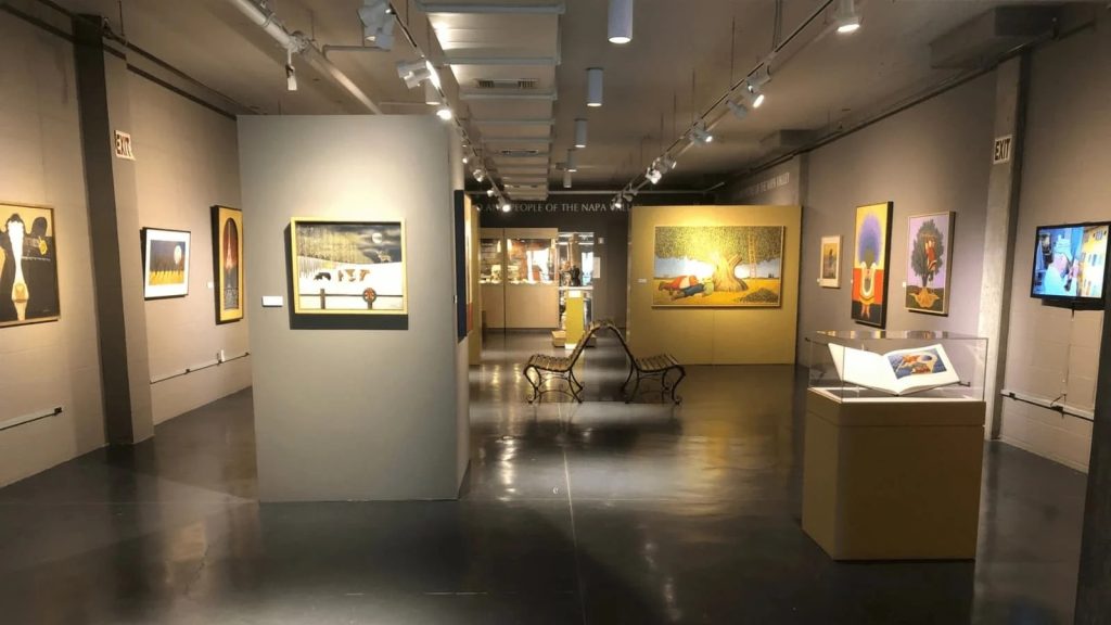 Interior view of the Napa Valley Museum Yountville displaying contemporary artworks on gray walls with track lighting and polished concrete floors in a modern gallery space.