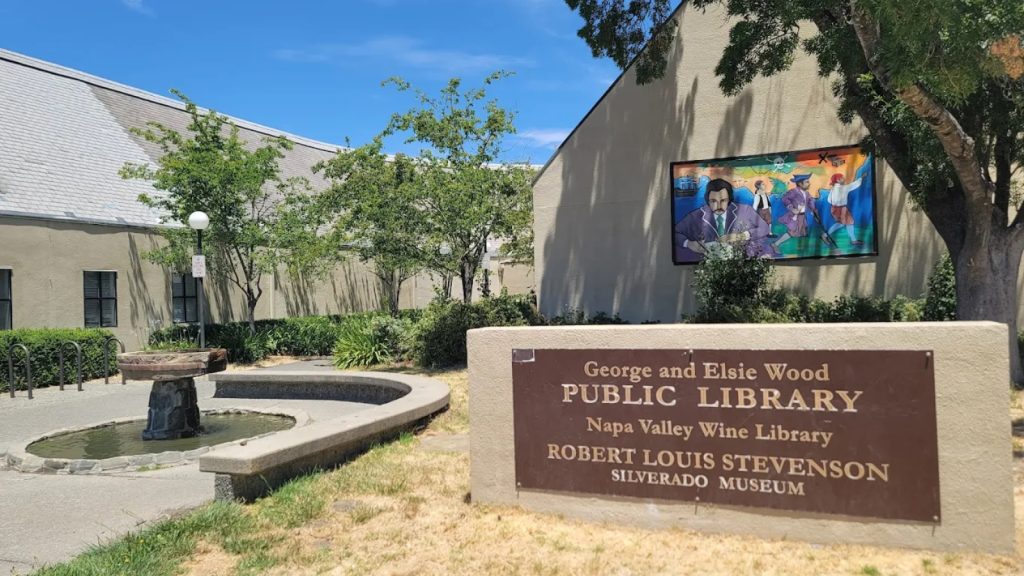 Exterior view of the Robert Louis Stevenson Museum at the George and Elsie Wood Public Library in St. Helena, featuring the bronze entrance sign and colorful mural on the building wall.