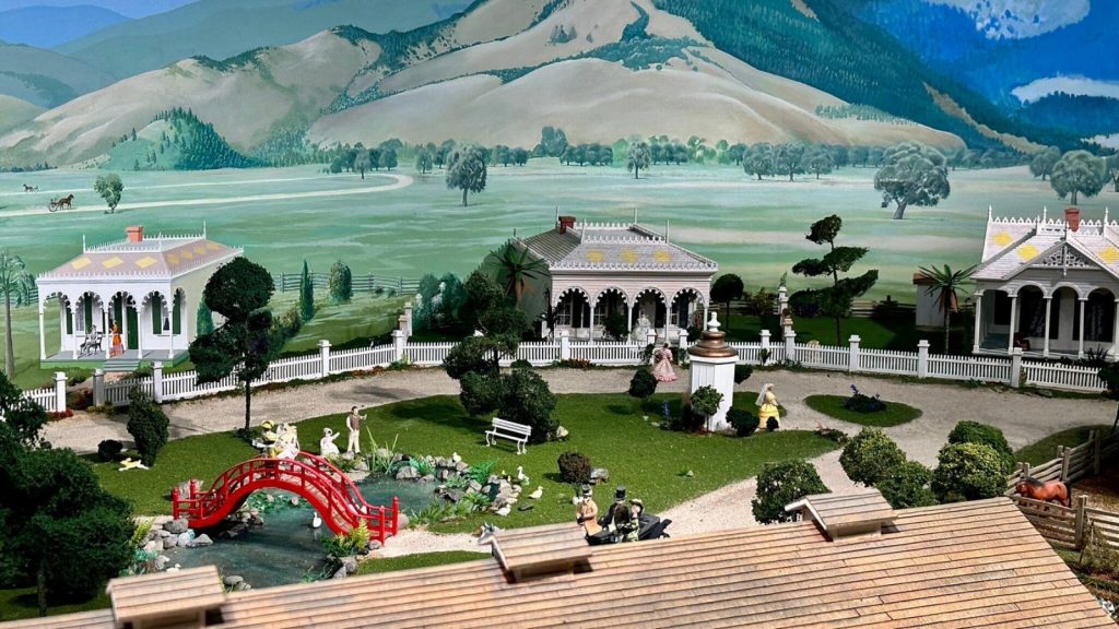 Historical diorama display at the Sharpsteen Museum featuring miniature Victorian buildings, a red bridge, landscaped gardens, and detailed figurines depicting 19th-century Calistoga life.