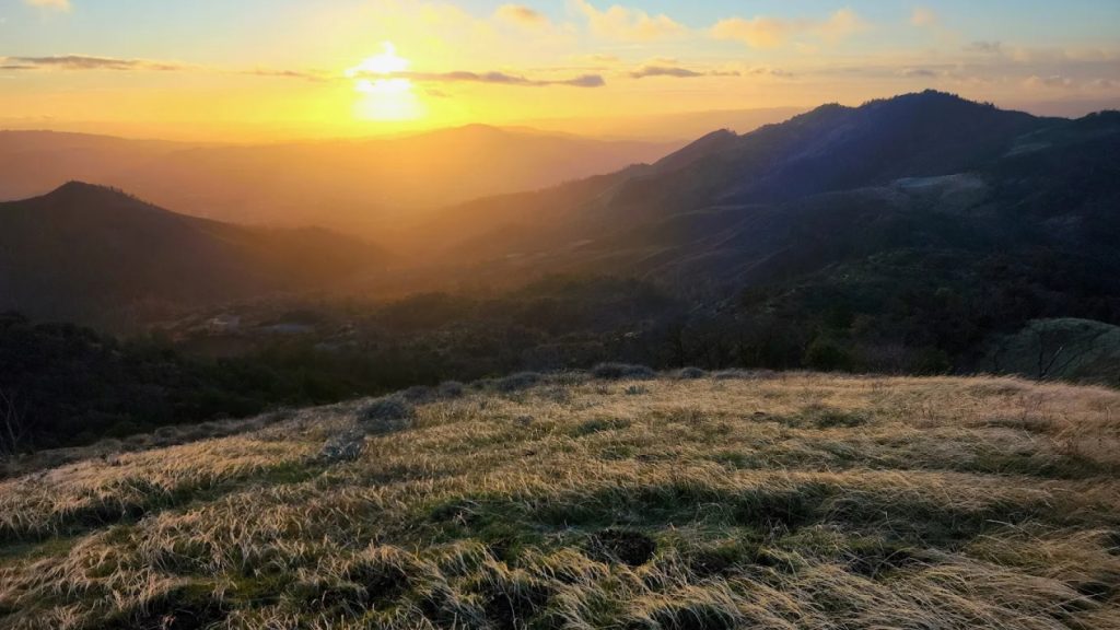 A golden sunset illuminates the rolling hills and grasslands at Sugarloaf Ridge State Park, showcasing the park's breathtaking panoramic views and natural beauty.