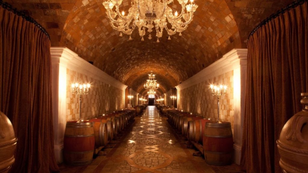 Elegant wine barrels lining the arched tunnels of Davis Estates Wine Cave with crystal chandeliers, wall sconces, and dramatic curtains creating a luxurious tasting atmosphere.