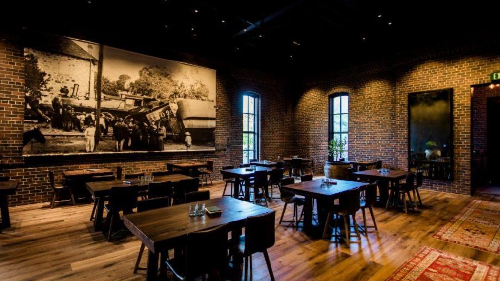 Charter Oak in St Helena features a modern restaurant interior with exposed brick walls, wooden tables, bar seating, historical photographs, and warm ambient lighting.
