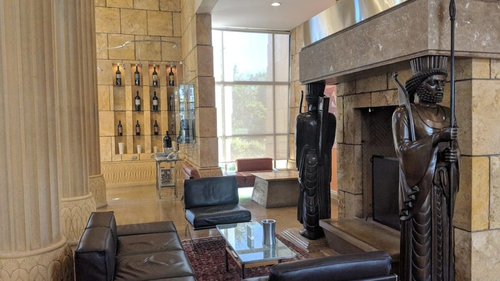 Darioush wine tasting room features luxurious décor with wine bottle displays, black leather seating, ornate sculptures, and stone architectural details creating an upscale ambiance.