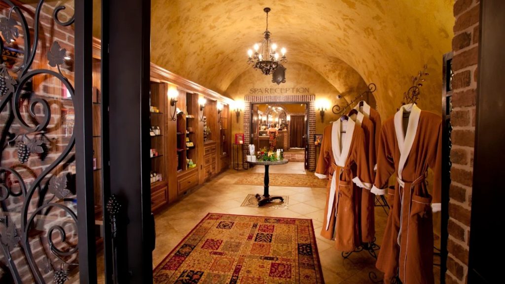 Spa Terra at The Meritage Resort showcases an elegant underground spa reception area with vaulted ceilings, luxury robes on display, crystal chandelier, and warm ambient lighting.
