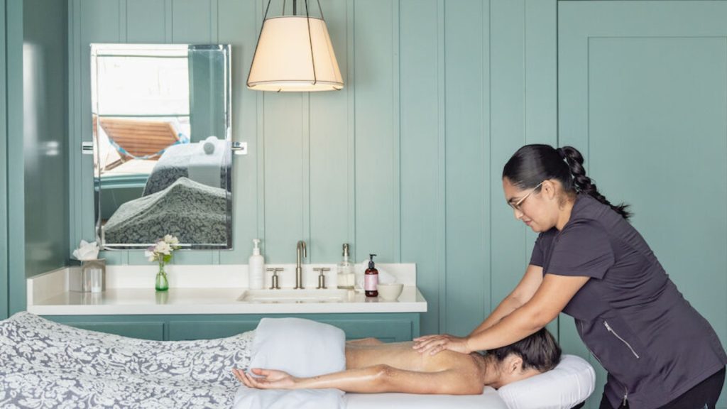 The Spa at Carneros features a spa therapist providing a professional massage treatment in a serene bedroom suite with mint green walls, modern fixtures, and relaxing ambiance.