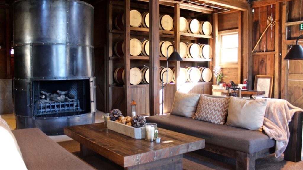 Davis Estates winery tasting room features wooden barrel storage displays, a modern fireplace, rustic wood furniture, and comfortable seating for wine tastings and guest experiences.