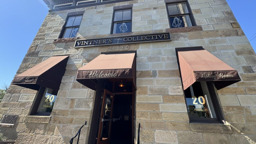 Vintners Collective storefront features a historic stone building with welcoming awnings, wine shop signage, and a tasting room entrance celebrating 20 years of wine appreciation.