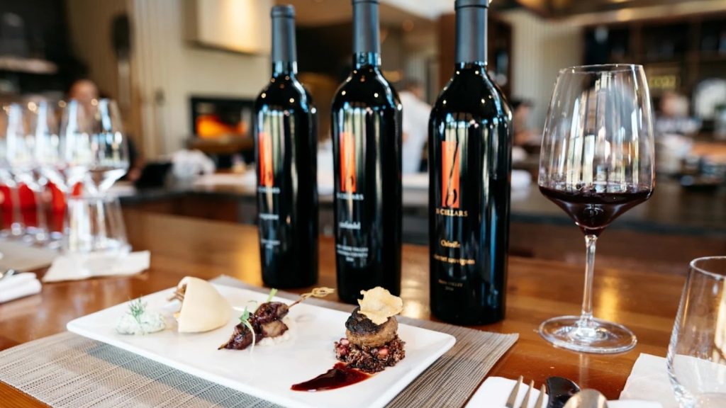 B Cellars wine and food pairing featuring three wine bottles, red wine glass, and elegant plated appetizers on wooden table