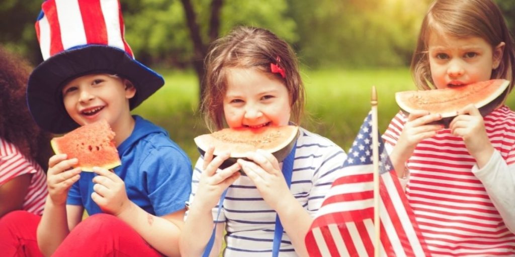 Children celebrating the 4th of July in Napa with patriotic outfits, watermelon, and American flags.