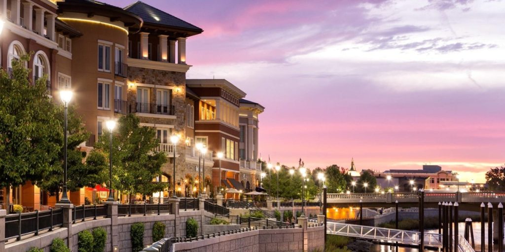 Downtown Napa: elegant historic buildings with warm lighting illuminate a riverside promenade at sunset under a vibrant purple and pink sky.