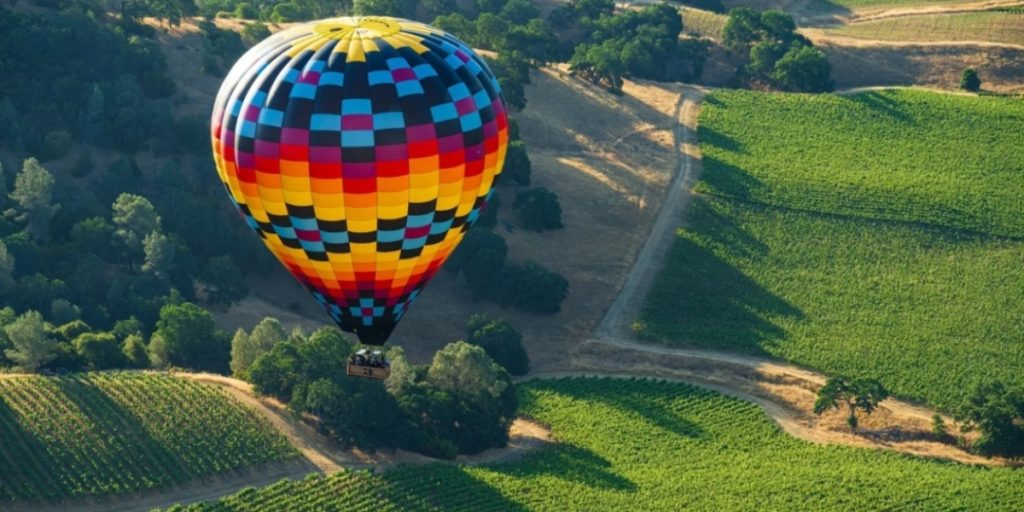 Aloft hot air balloon flying above Napa Valley vineyards with vibrant red, yellow, and blue checkered pattern floating over lush grapevines and scenic wine country landscape.