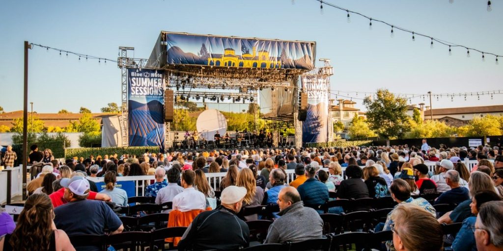 Live Music at Blue Note Napa Summer Sessions – outdoor concert venue with large stage, crowd of spectators seated at tables, string lights, and professional sound setup during evening performance