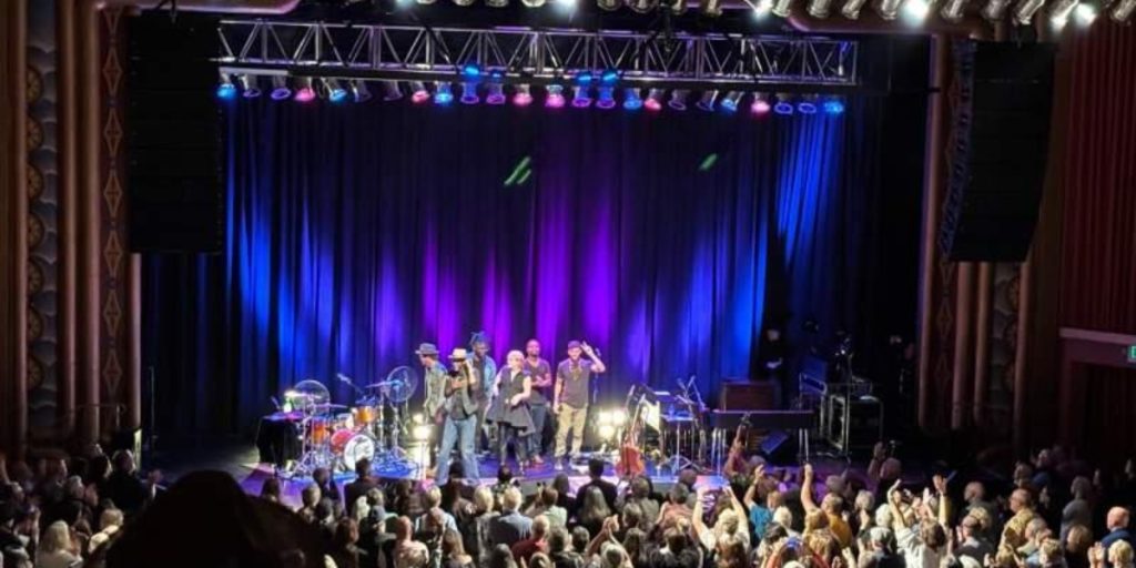 Napa Music Hall Events featuring a live band performing on stage with vibrant blue and purple lighting, dramatic curtains, and an energetic crowd of audience members enjoying the concert.