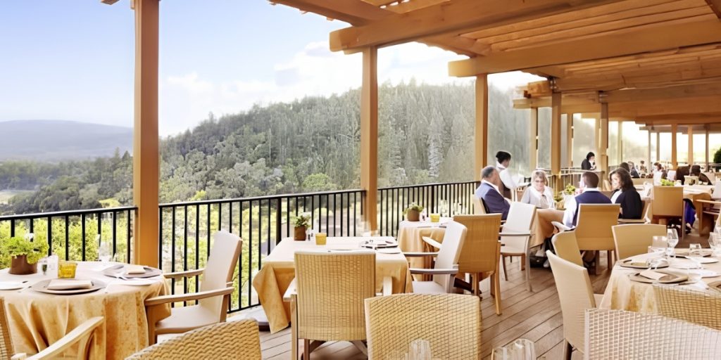 Outdoor Dining at an elegant hilltop restaurant with panoramic valley and forest views, featuring white tablecloths, comfortable seating, and diners enjoying a sophisticated meal on a scenic terrace.